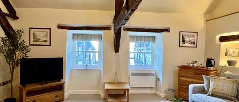 Un salón acogedor con vigas de madera a la vista, un televisor, un sofá y dos ventanas con cortinas.