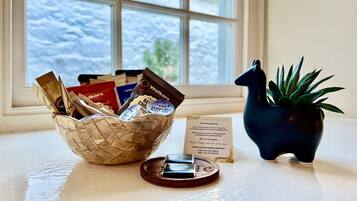 A window with a view of snow-covered ground, a wicker basket with various items, a small potted plant, and a welcome card on a table.