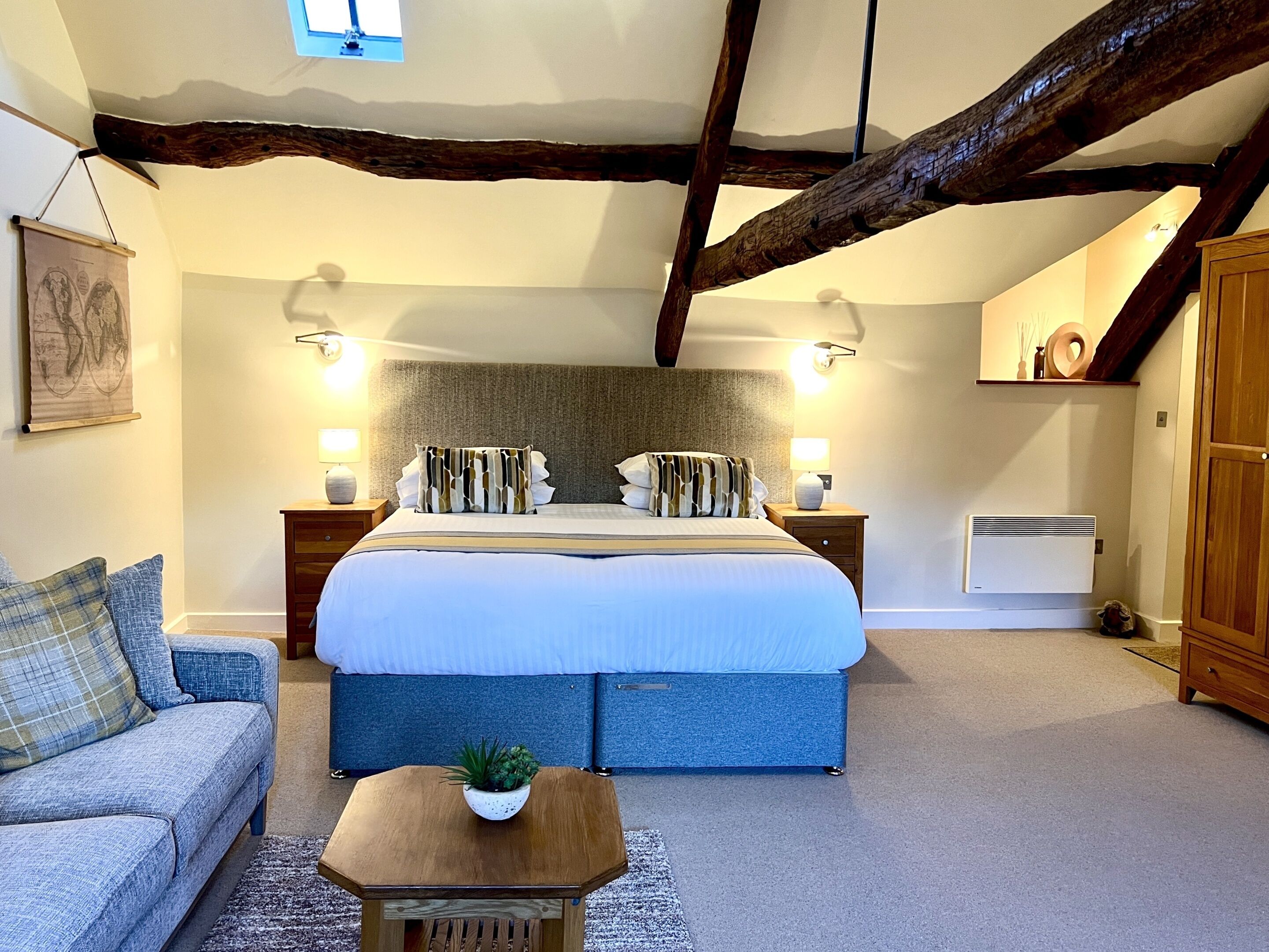 A bedroom with a large bed, two bedside tables, a wooden bench, a small table with a plant, a sofa, and a wooden wardrobe.