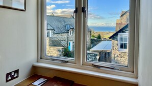 A room with a large window overlooking a stone building and a view of the sea. - Castle Cottage Inn (Harlech)