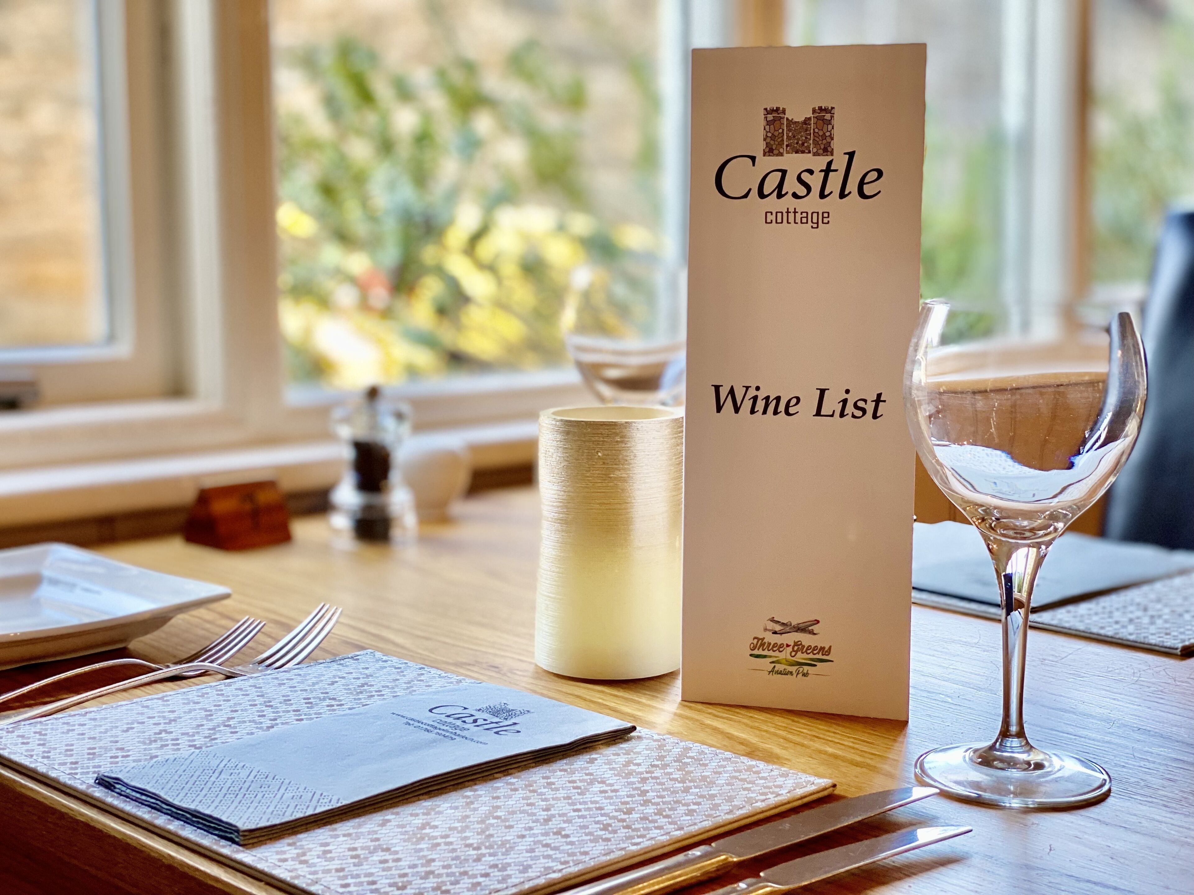 A table set with a menu, a wine glass, and a candle, with a window view in the background.