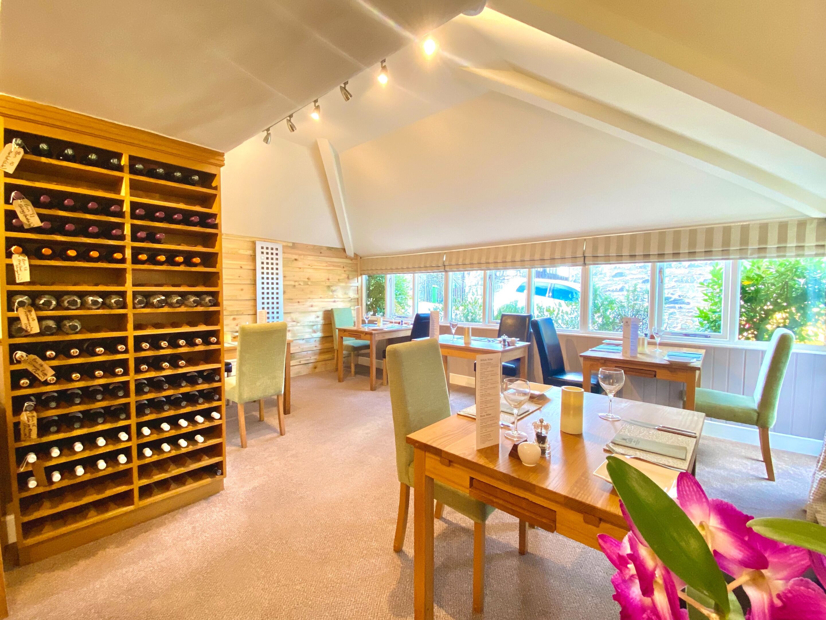 A room with a wine rack, dining table, chairs, and a view of greenery outside.