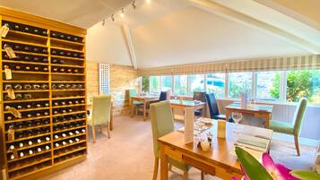 A room with a wine rack, dining table, chairs, and a view of greenery outside.