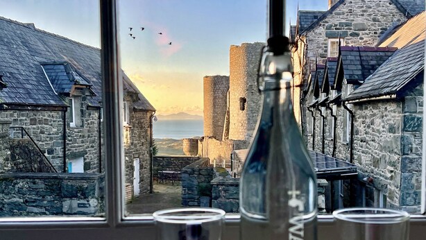 A bottle of water and glasses on a table with a view of stone buildings and a distant landscape. - Castle Cottage Inn (Harlech)