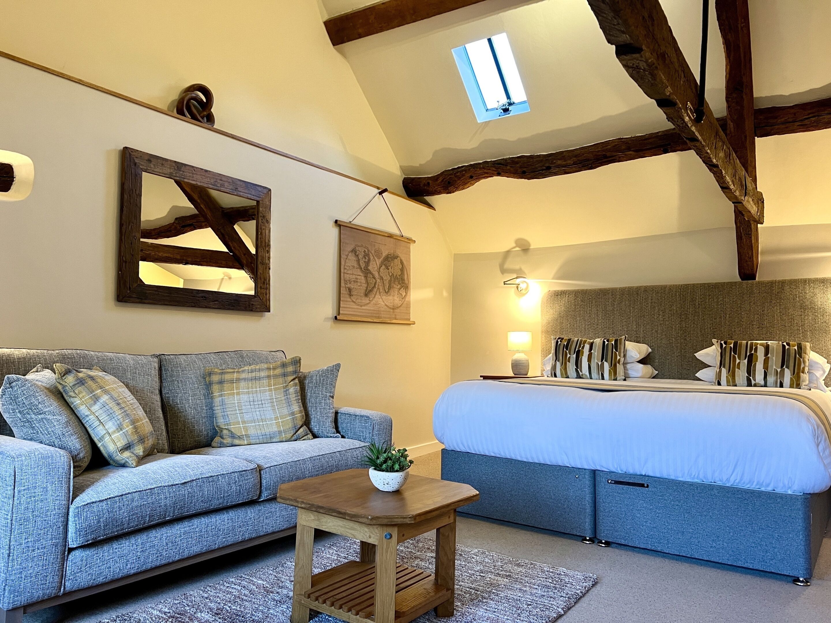 A bedroom with a bed, a sofa, a small table, a window, and a wall-mounted picture.