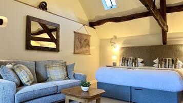 A bedroom with a bed, a sofa, a small table, a window, and a wall-mounted picture.