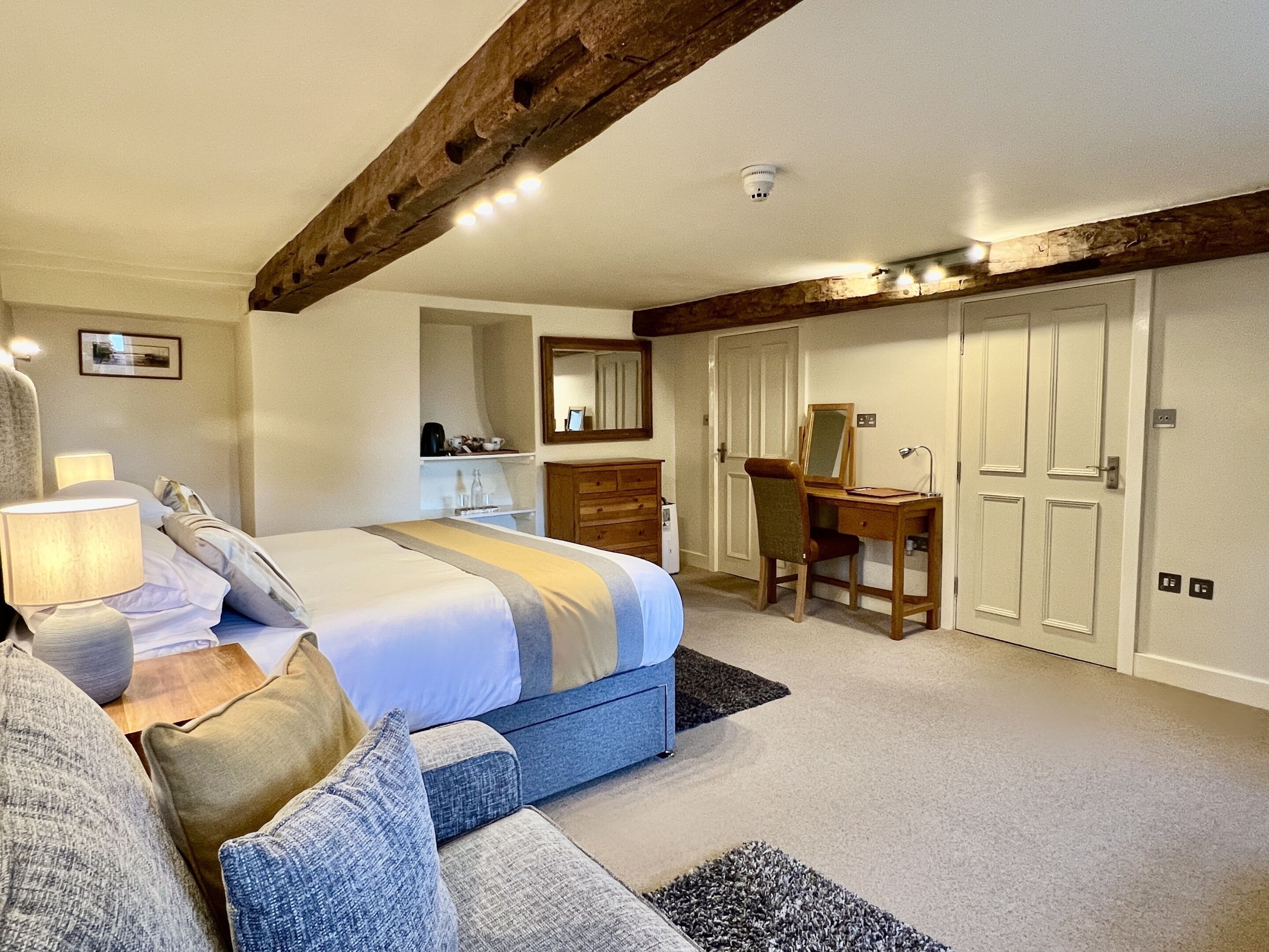 A bedroom with a bed, bedside table, lamp, dresser, desk, chair, mirror, and wardrobe.