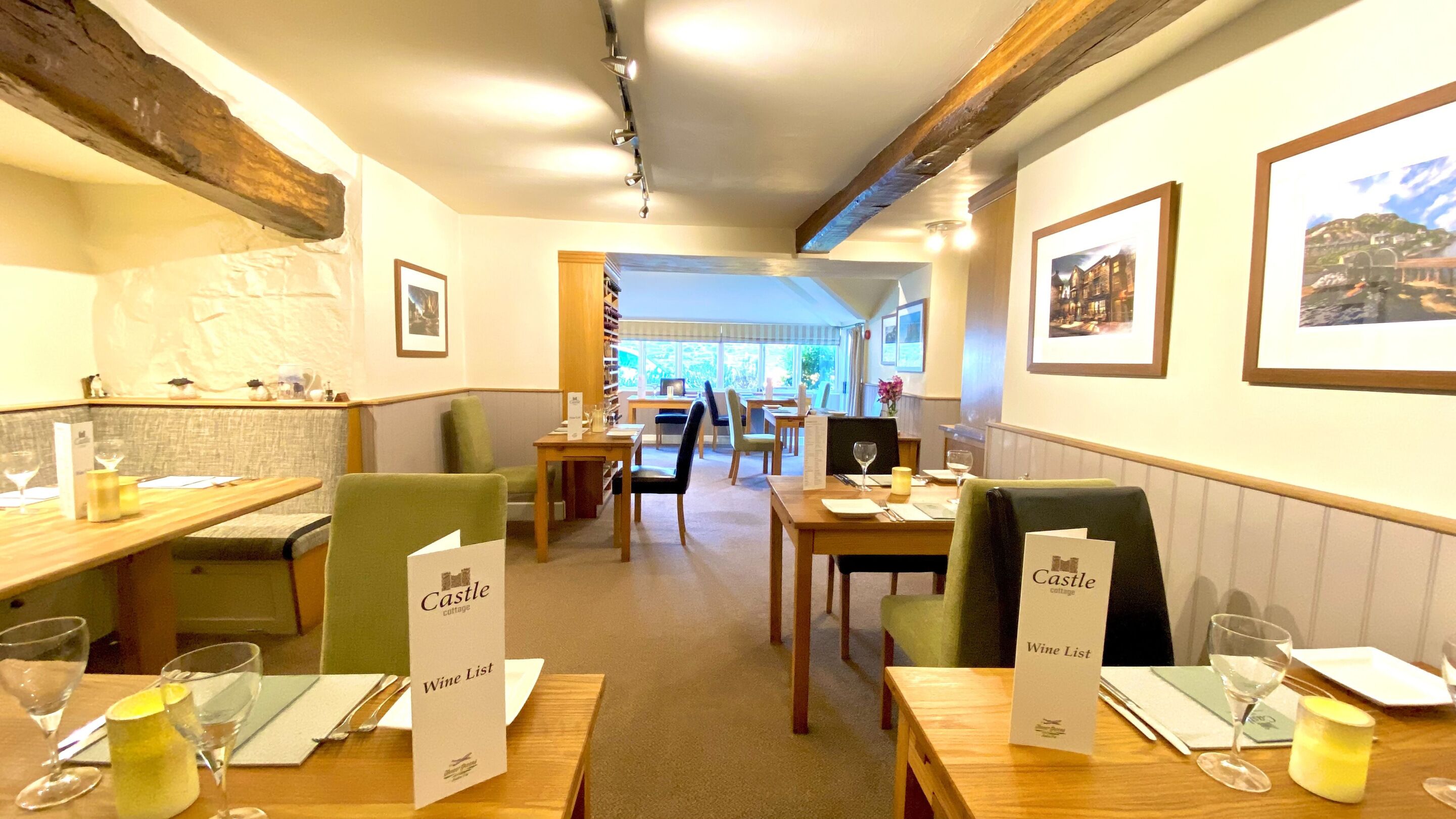 A restaurant with wooden tables and chairs, a wine list sign, framed pictures on the walls, and a view through the window.
