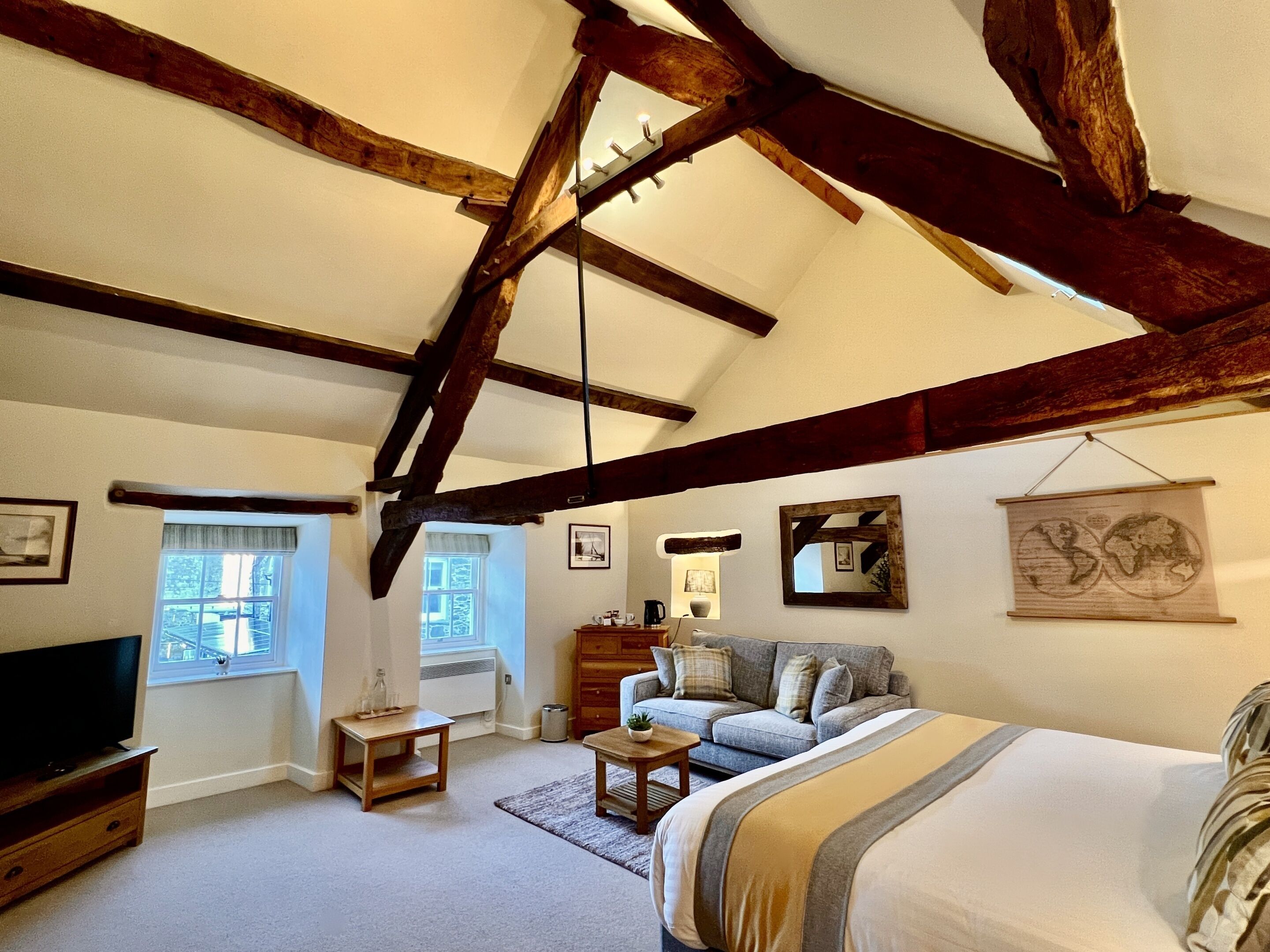 A cozy bedroom with exposed wooden beams, a large bed, a television, and a window with curtains.