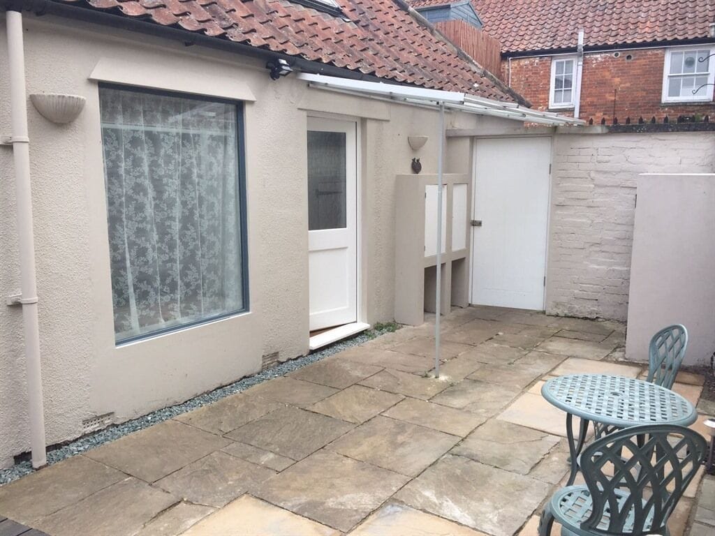A patio with stone flooring, a white door, and a window with a patterned curtain.