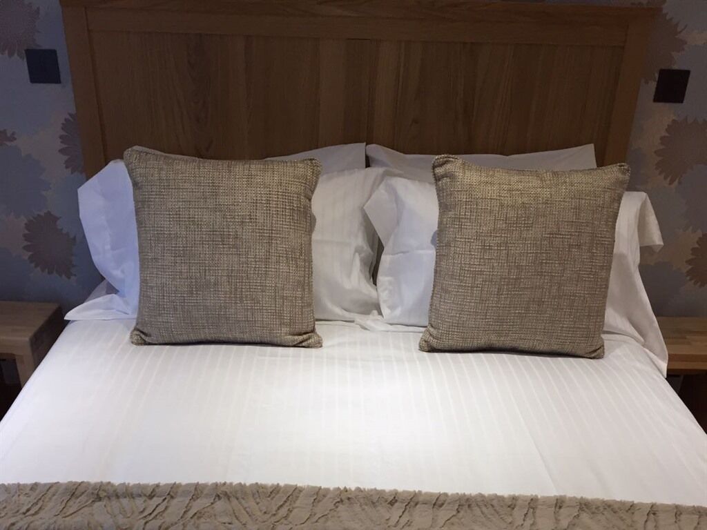 Una cama con cabecera de madera, dos almohadas color beige y una colcha blanca.