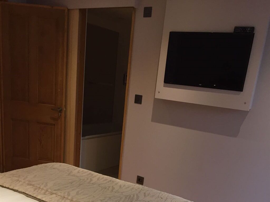 A room with a bed, a wooden door, and a mounted television on the wall.