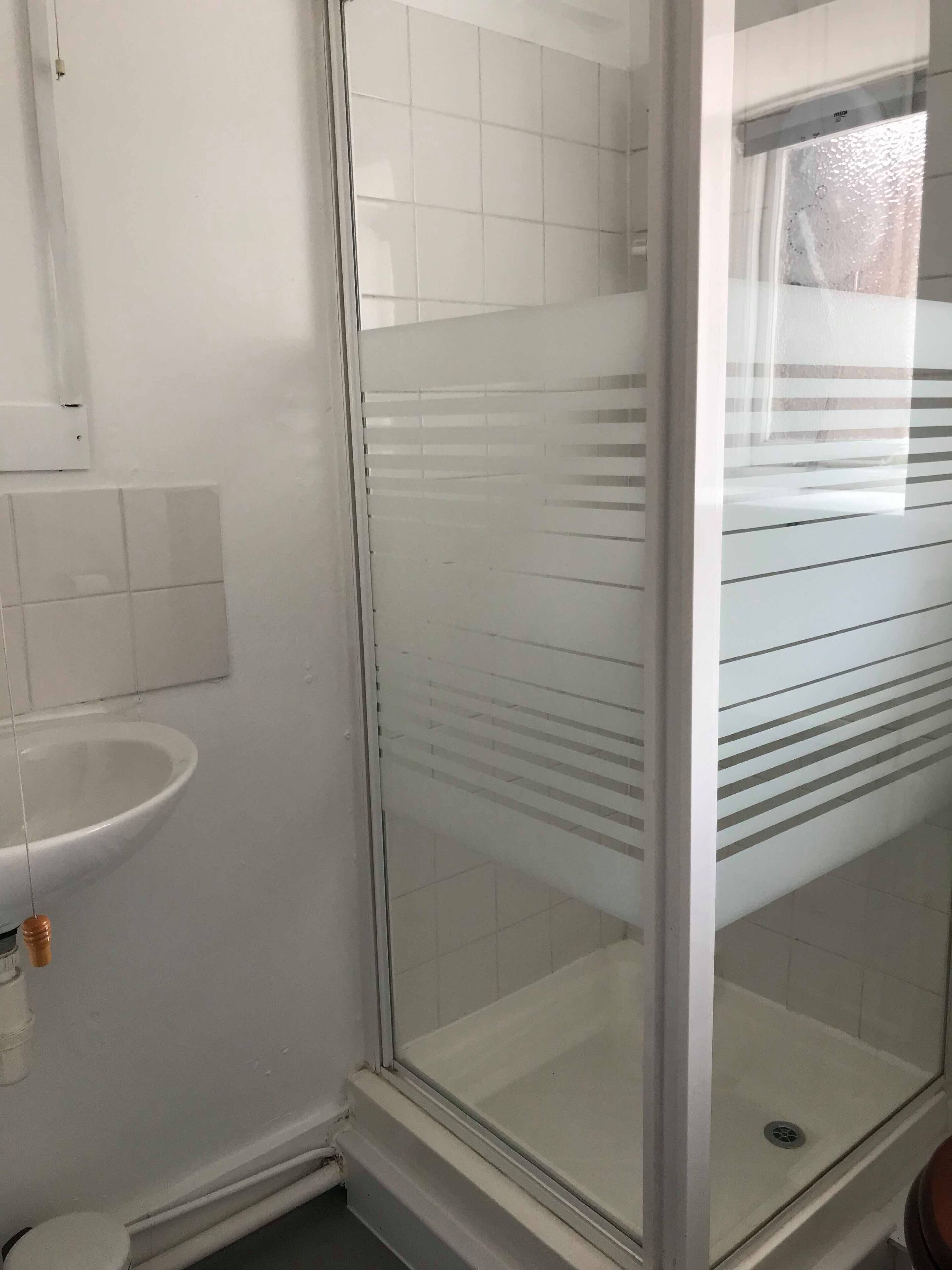 A bathroom with a glass shower enclosure, a white sink, and a tiled floor.