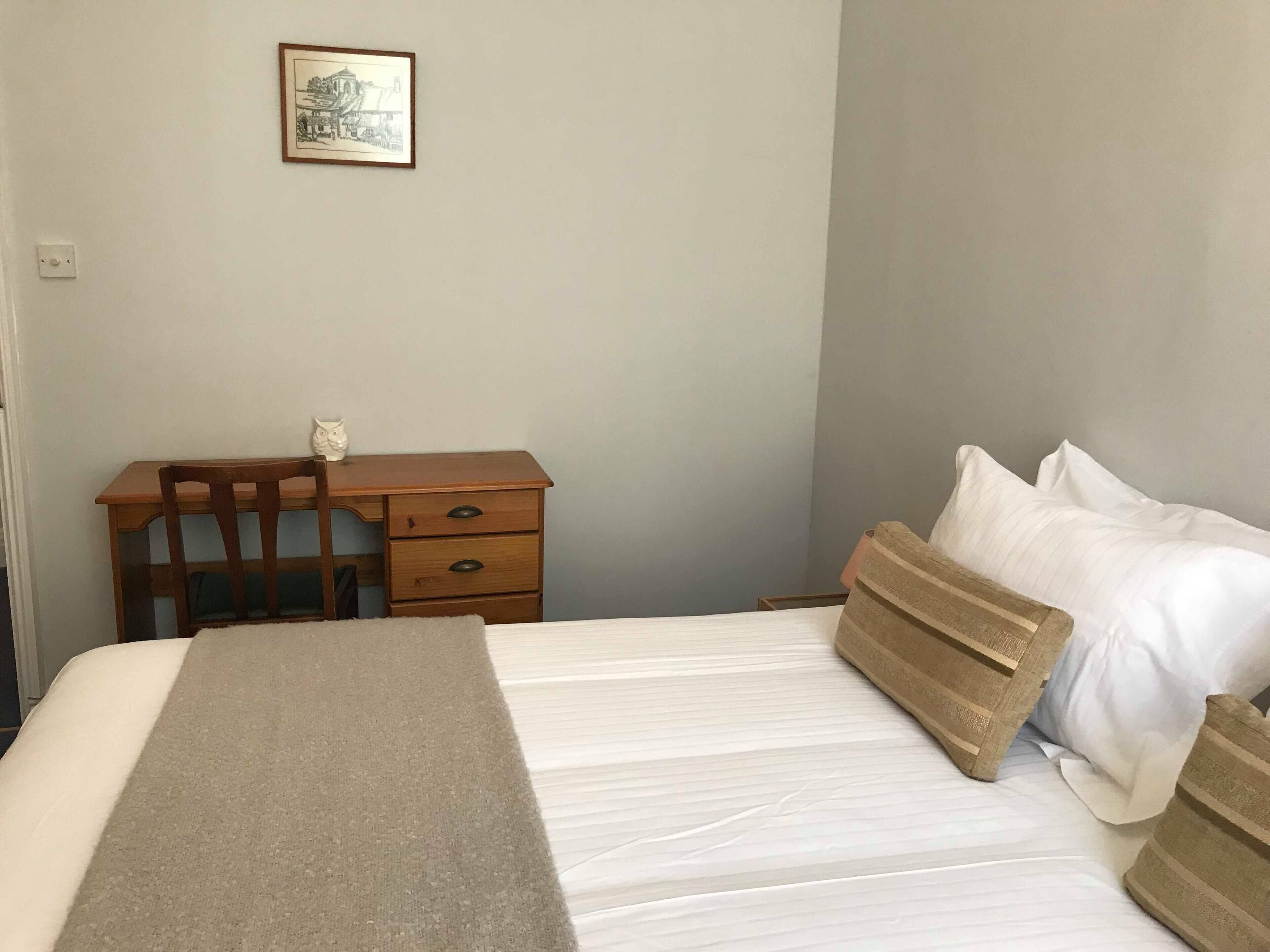 A bedroom with a bed, a wooden desk, a chair, a nightstand, and a framed picture on the wall.