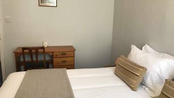 A bedroom with a bed, a wooden desk, a chair, a nightstand, and a framed picture on the wall.