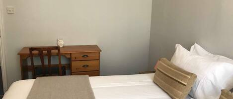A bedroom with a bed, a wooden desk, a chair, a nightstand, and a framed picture on the wall.