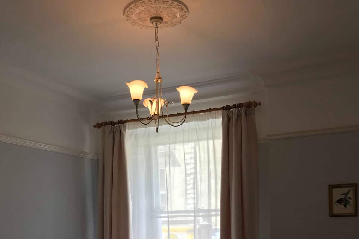 A hotel room with a bed, a chair, a chandelier, and a window with curtains.