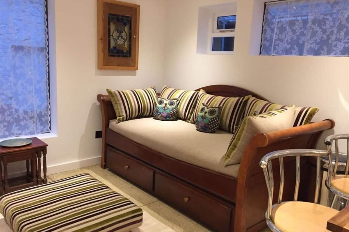 A cozy room with a wooden sofa, striped ottoman, and a metal chair.