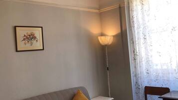 Una habitación con un sofá gris, una silla de madera, una araña, un cuadro enmarco y una lámpara.