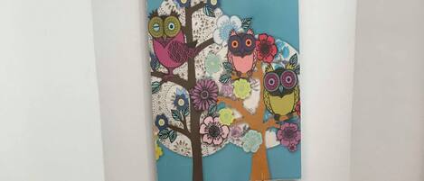A room with a white fireplace, a white mantel, and a colorful painting of owls and flowers above it.