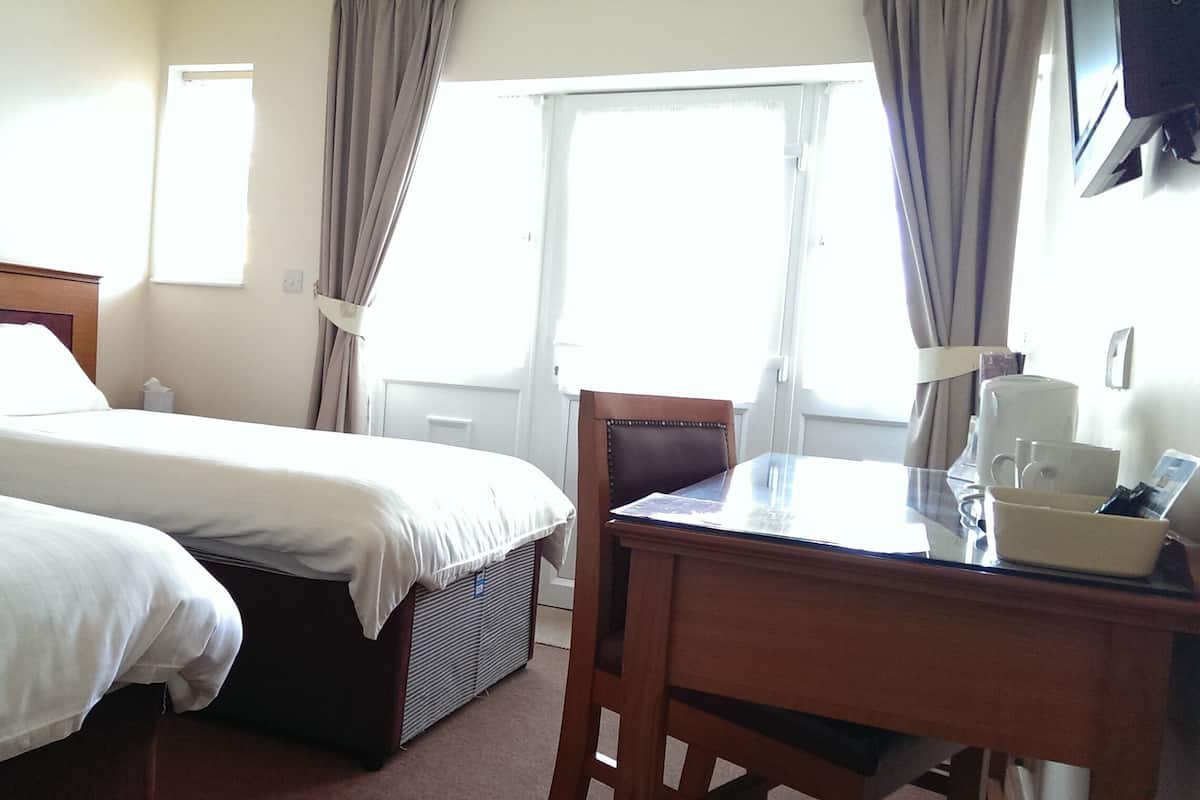 A hotel room with two beds, a desk with a coffee maker, and a window with curtains.