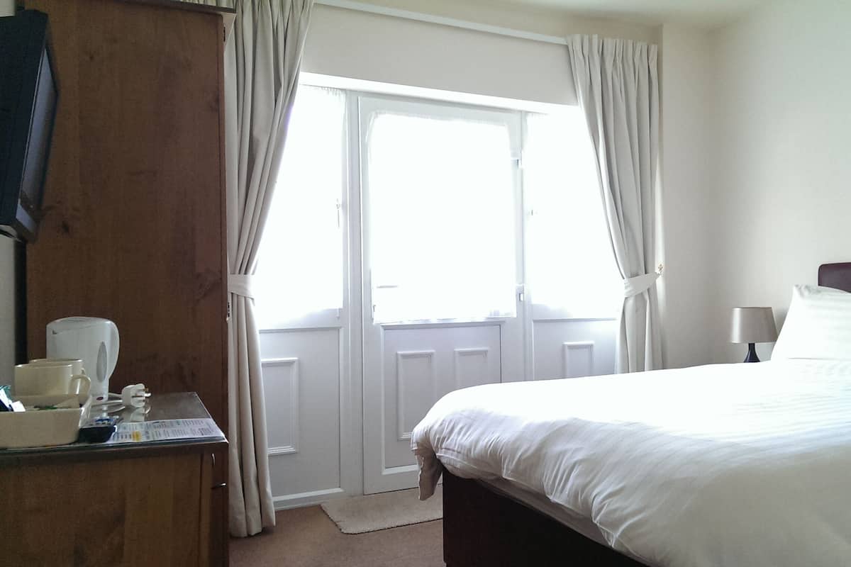 A hotel room with a bed, a desk with a coffee maker, and a view through a door.