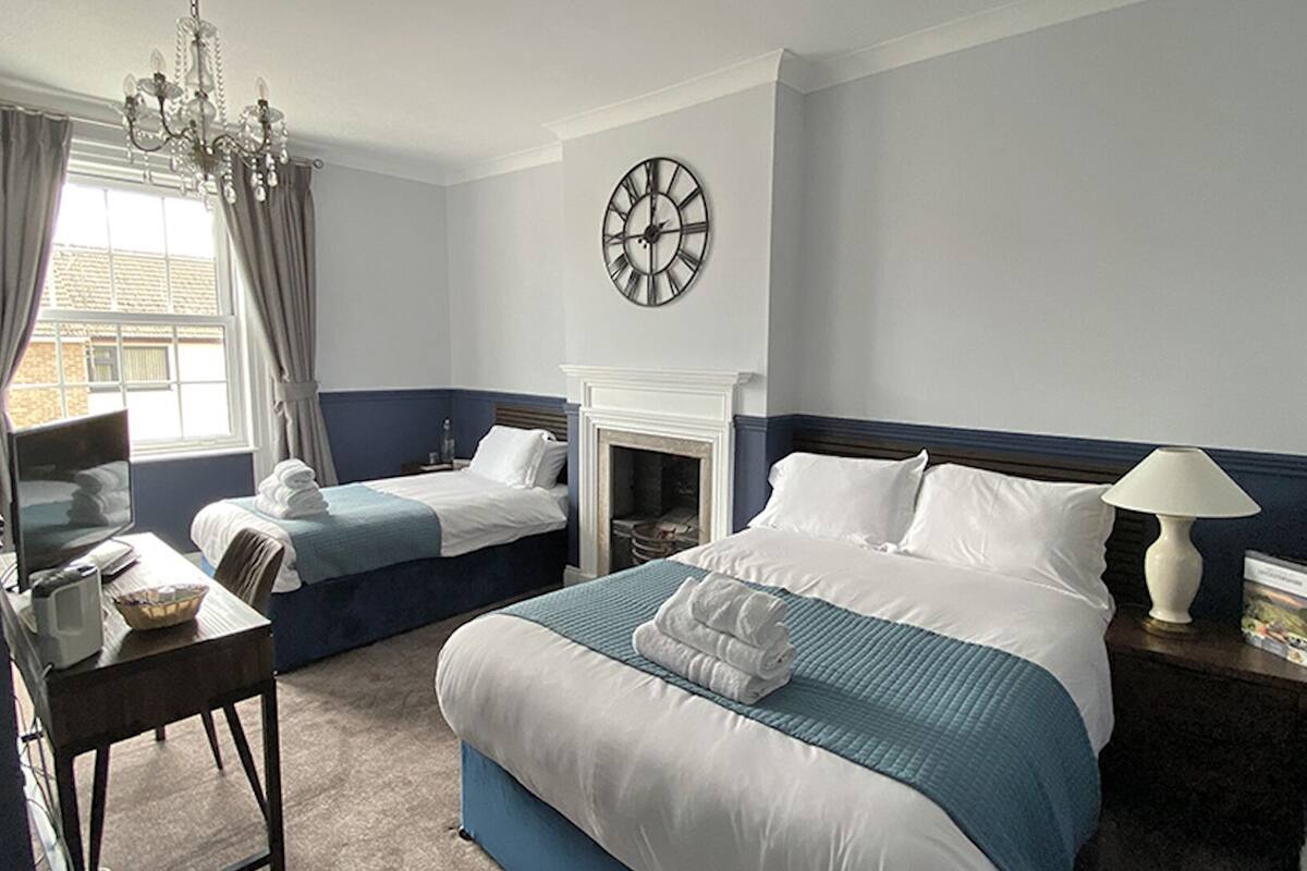 A hotel room with two beds, a chandelier, a clock, and a fireplace.