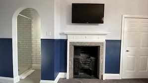 Una habitación con chimenea, un televisor colocado encima y una puerta a la derecha.