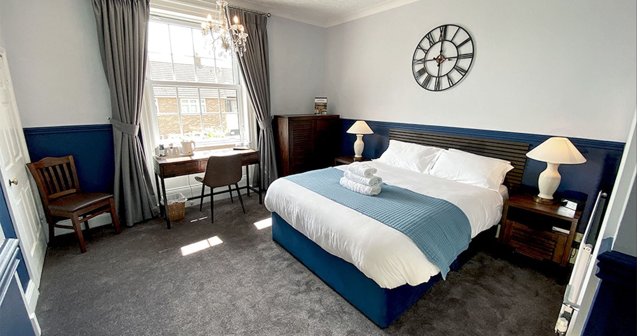 A neatly arranged bedroom with a bed, two bedside tables, a desk, and a chair.