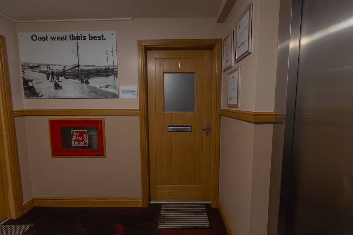 A hallway with a wooden door, a framed poster, and a fire exit sign.
