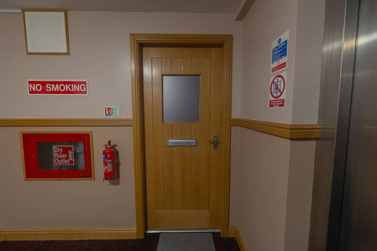 A wooden door with a fire extinguisher and a 'No Smoking' sign on the wall.