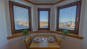Comedor con una mesa preparada para dos, flanqueado por tres ventanas con persianas, cada una con una pequeña planta.