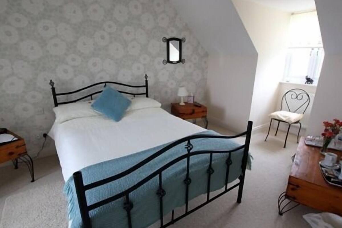 A bedroom with a bed, a nightstand, a chair, a dresser, and a mirror on the wall.