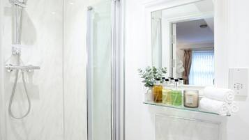 A modern bathroom with a glass shower enclosure, a glass shelf with toiletries, and a mirror reflecting a room with a window and curtains.