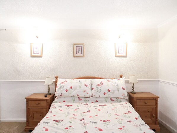 Een slaapkamer met een bed, twee nachtkastjes en drie aan de muur bevestigde fotolijstjes.
