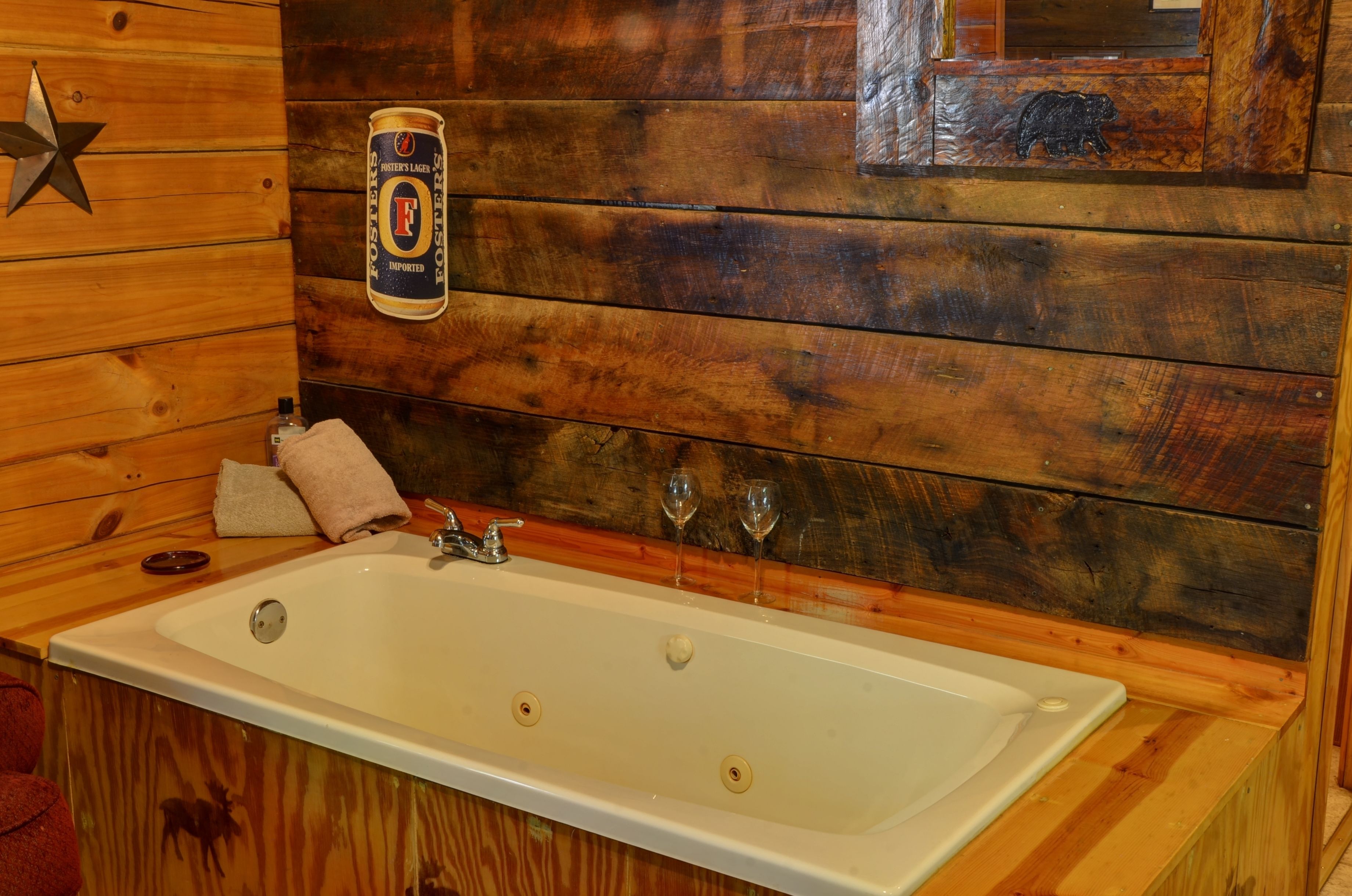 A wooden cabin interior with a large bathtub, a star decoration, a bear cutout, and a beer can on the wall.