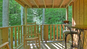 A wooden deck with a rocking chair and a bar stool, surrounded by trees. - Panther Creek Cabins (Cherokee)