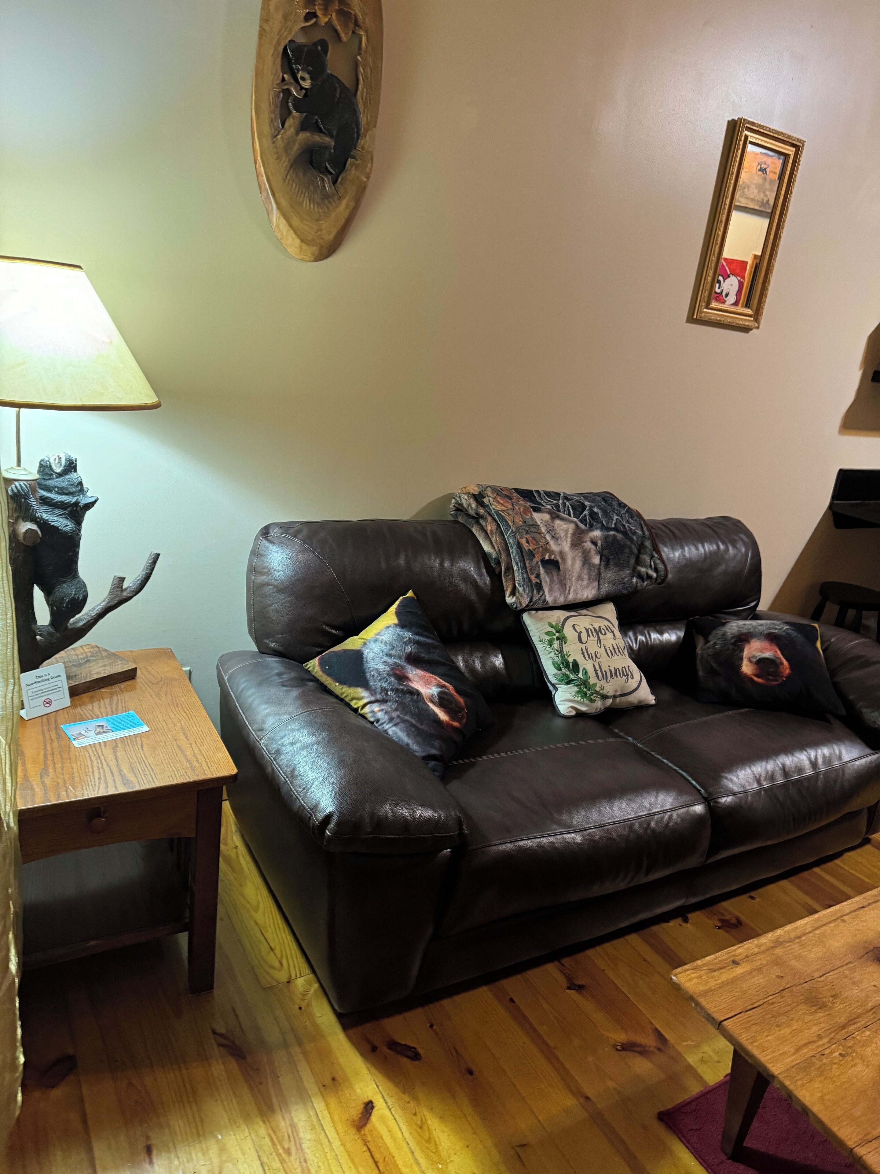 Un salón con un sofá de cuero marrón, una mesita de madera con una lámpara y una escultura de oso.
