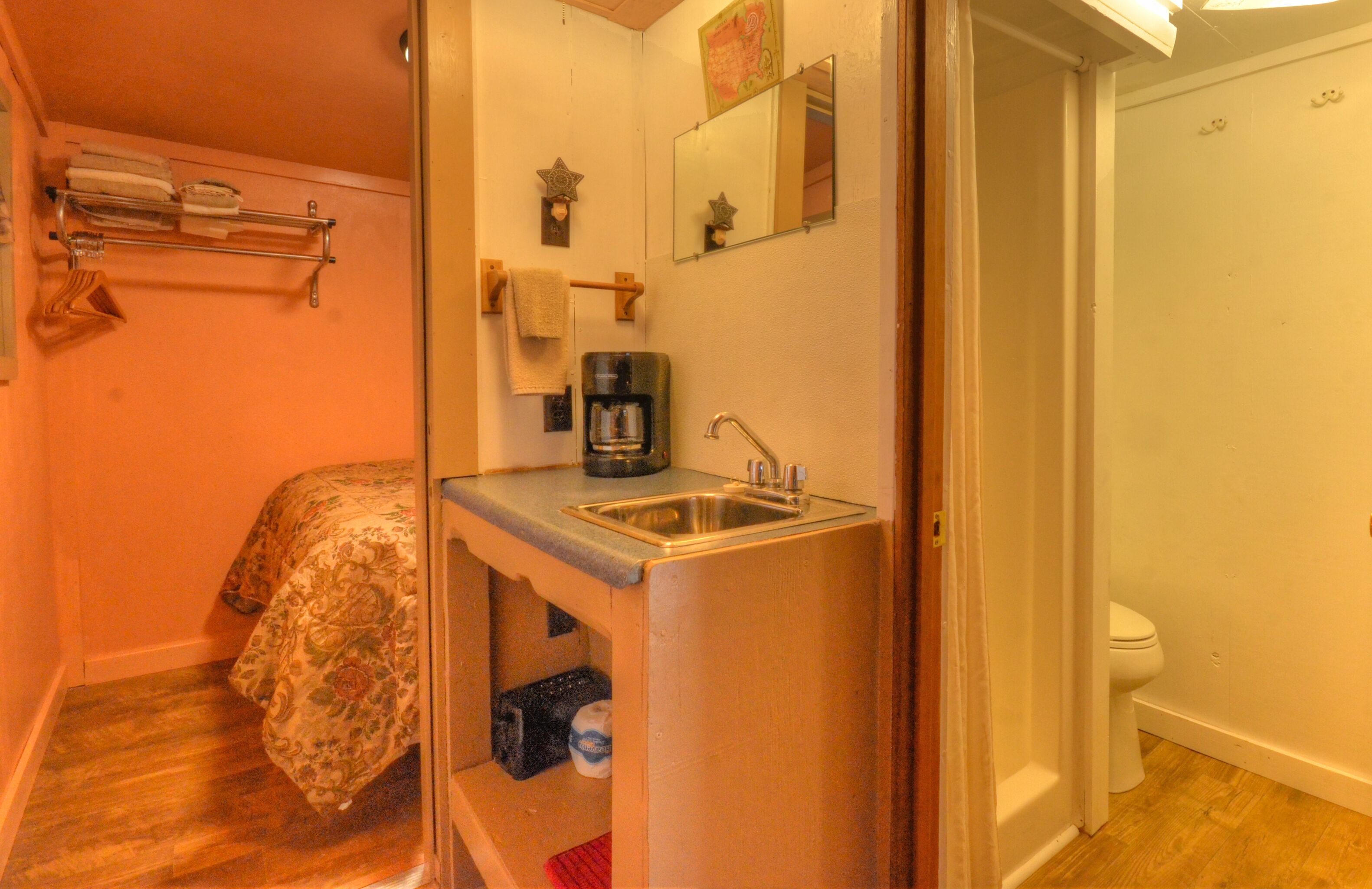 Een compacte slaapkamer met een bed, een kleine kitchenette met een spoelbak en koffiezetapparaat, en een toilet.