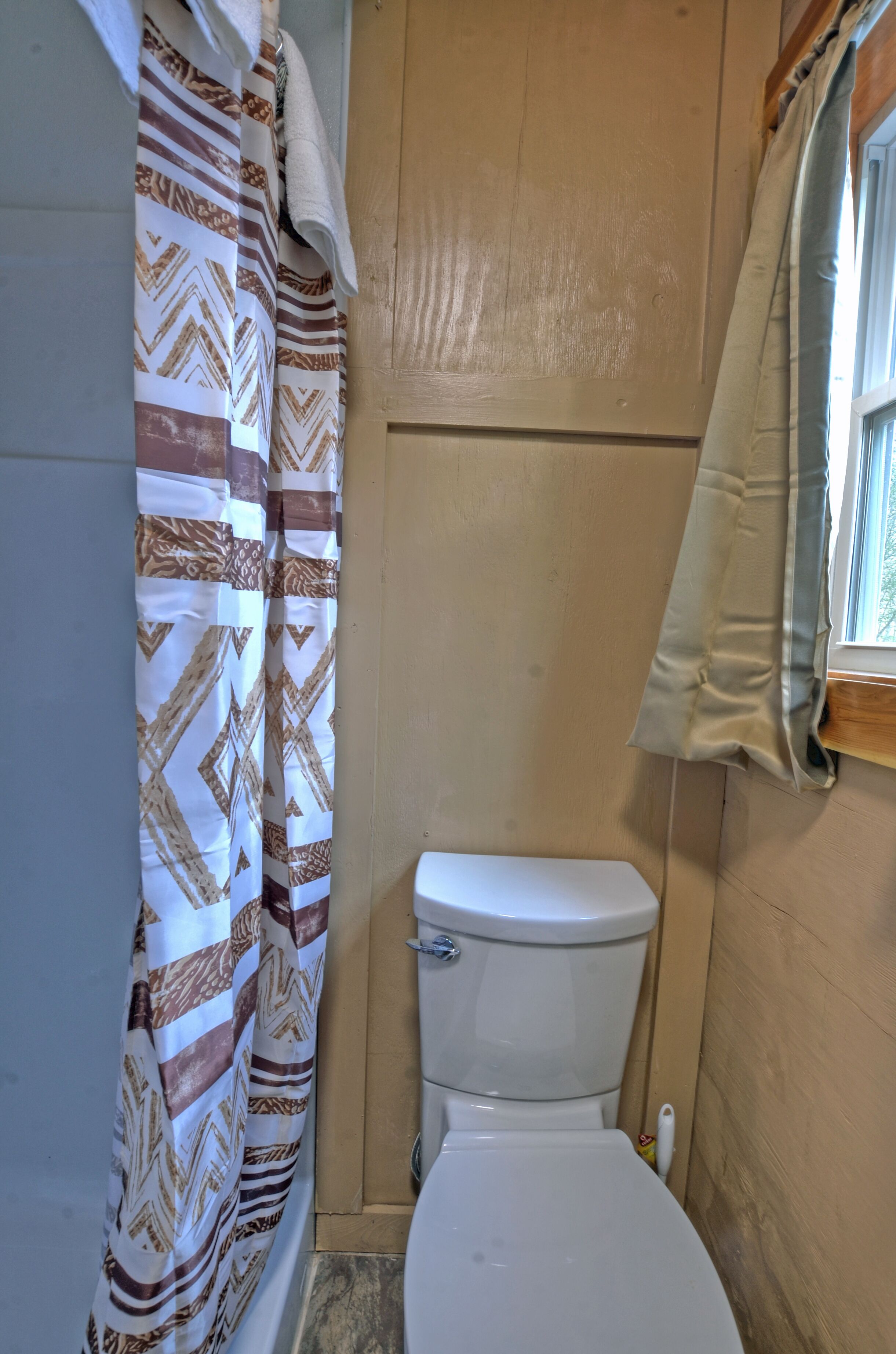 Um banheiro com cortina de chuveiro estampada, vaso sanitário branco e paredes de madeira.