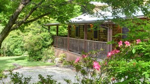 A wooden cabin with a balcony, surrounded by lush greenery and flowering plants. - Panther Creek Cabins (Cherokee)