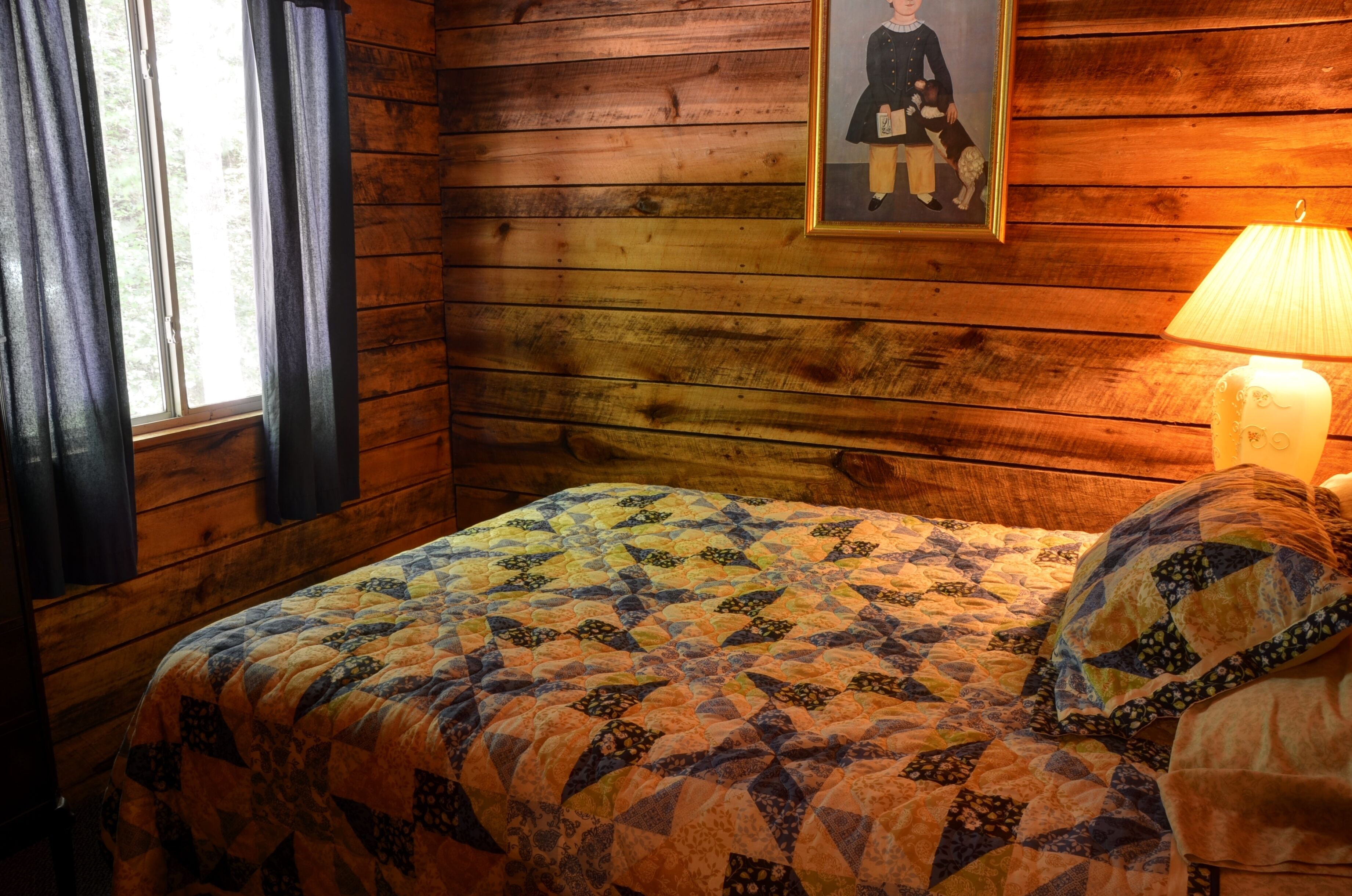Habitació d'una cabana de fusta amb un llit, un quadre al mur i una làmpada.
