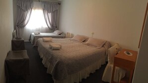 A hotel room with two beds, a small table, a chair, and a window with curtains. - Hotel San Jorge (Junin de los Andes)