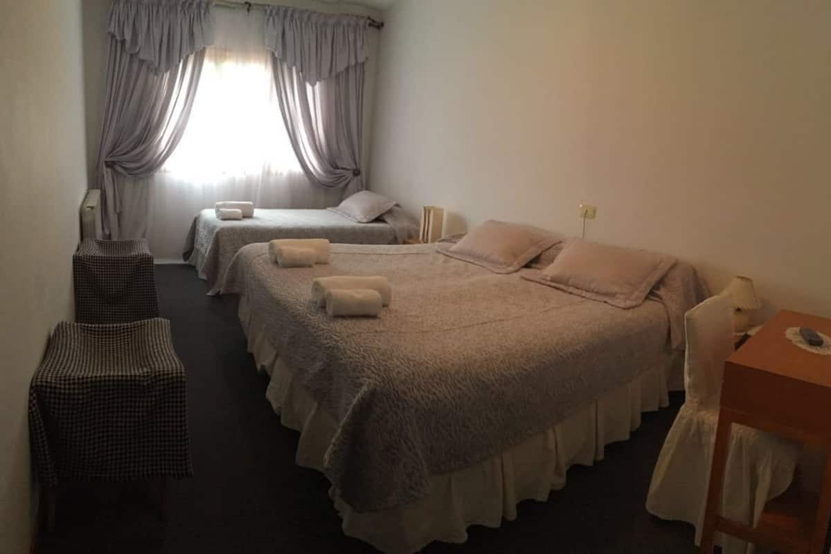 Une chambre d’hôtel avec deux lits, une petite table, une chaise et une fenêtre avec des rideaux.