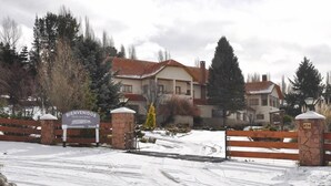 A snow-covered entrance to a residential area with a 'Bienvenidos' sign, a wooden gate, and a stone pillar with the number 674. - Hotel San Jorge (Junin de los Andes)