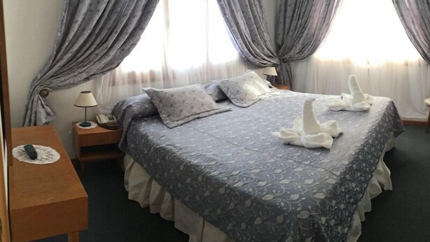 A hotel room with a bed, a nightstand, a lamp, and a window with curtains. - Hotel San Jorge (Junin de los Andes)