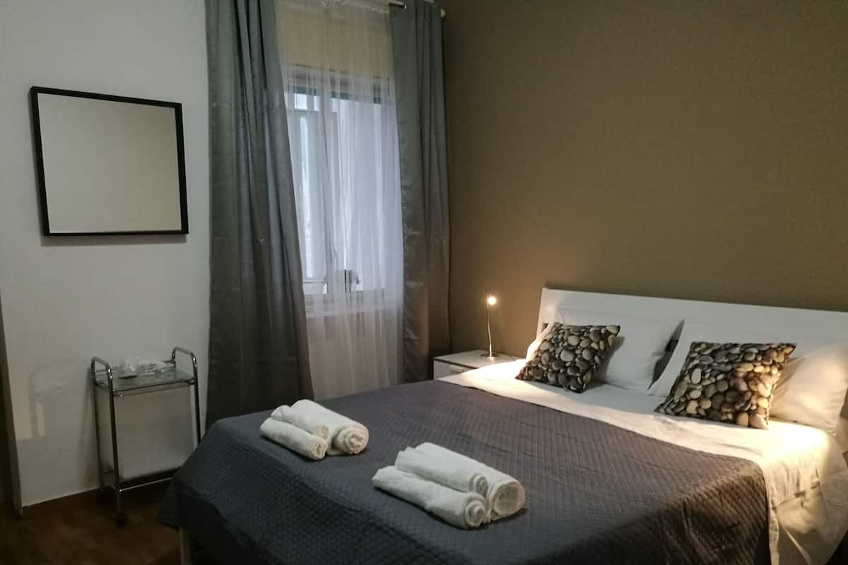 A neatly made bed with two rolled towels, a bedside lamp, and a nightstand with a small table.