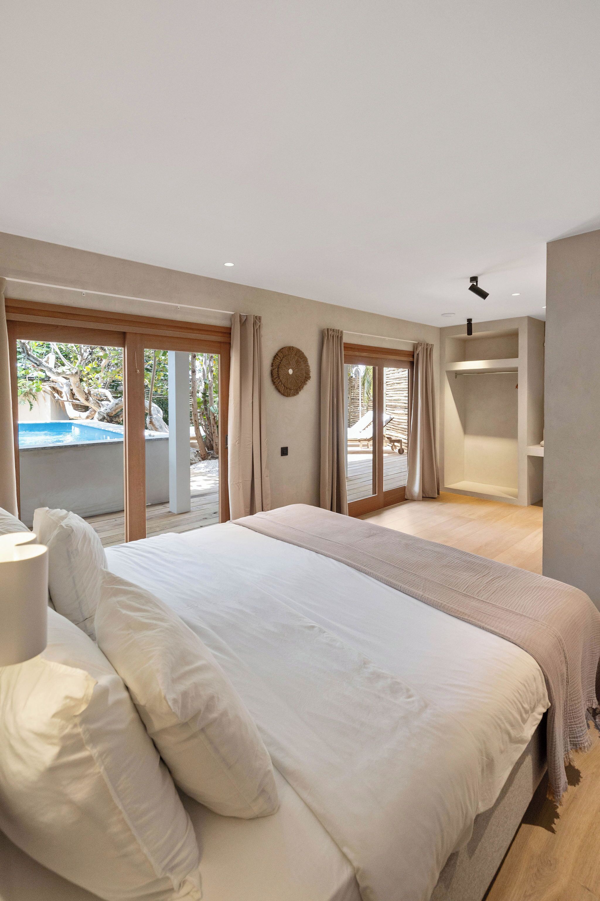 A bedroom with a large bed, a walk-in closet, and a sliding glass door leading to a pool area.