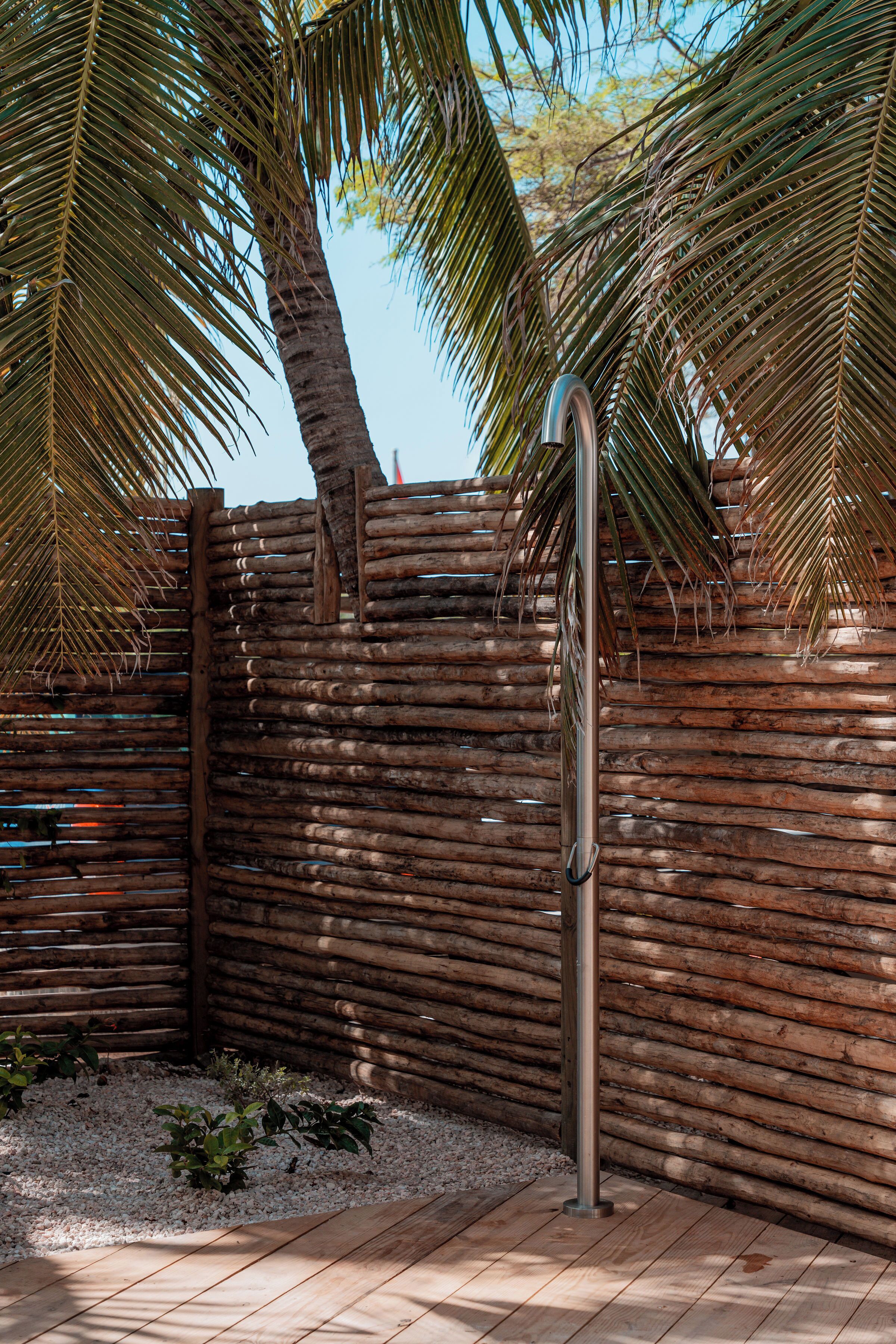 A wooden fence with a metal gate, palm trees, and a gravel area.