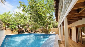 Piscina con terraza de madera y sillas de descanso, rodeada de exuberante vegetación y árboles.